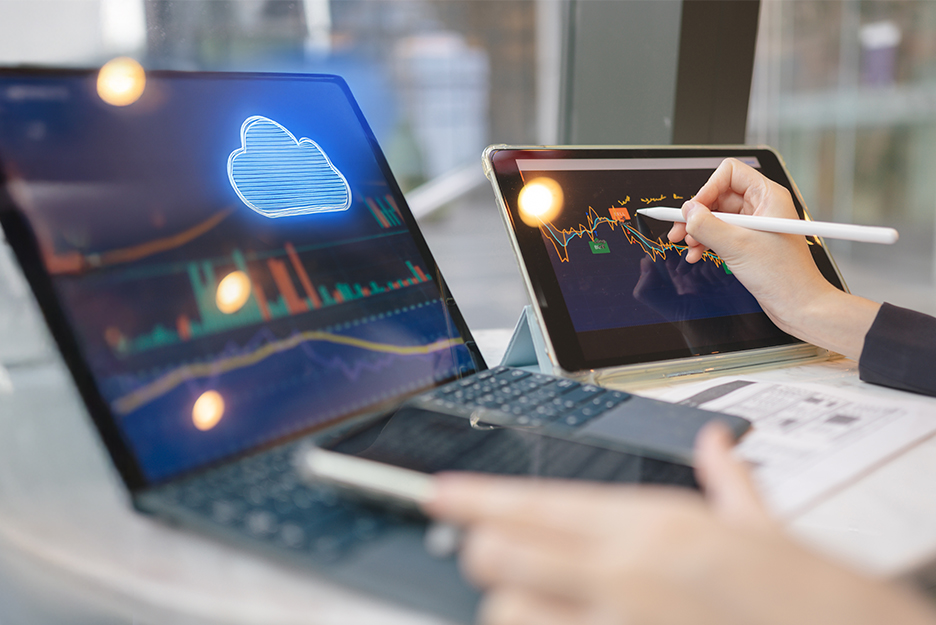 Laptop and tablet with cloud icon and financial charts, hand drawing a curve on the screen with a stylus.