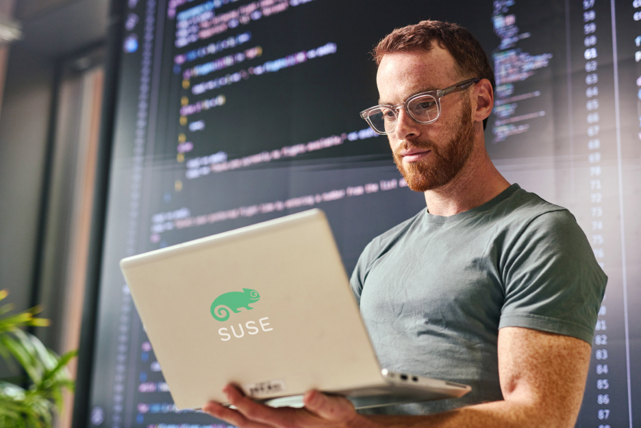 IT professional working on a laptop in front of screens displaying code. The image represents a modern cloud operating system upgrade with SUSE Linux.
