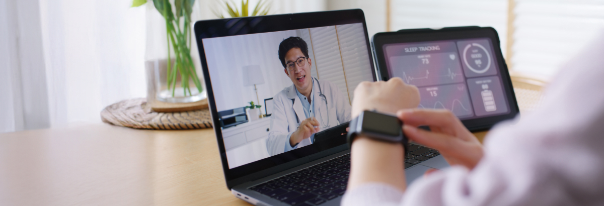 Eine Person mit einer Smartwatch sitzt vor einem Laptop und wird online von einem Arzt beraten