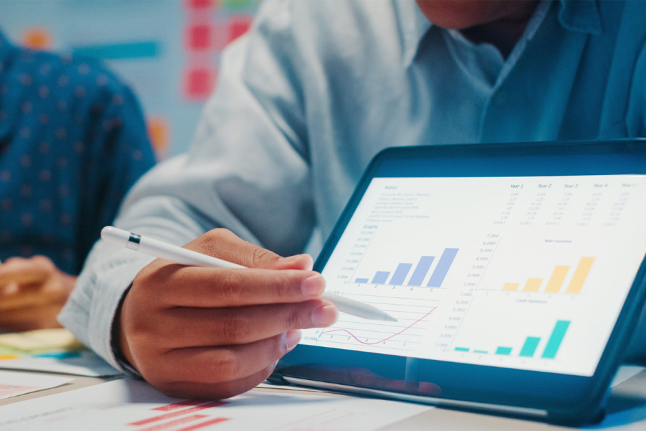 Person analysiert Cloud-Kosten und Geschäftsdaten auf einem Tablet mit Diagrammen und KPI-Dashboards in einer modernen Büroumgebung
